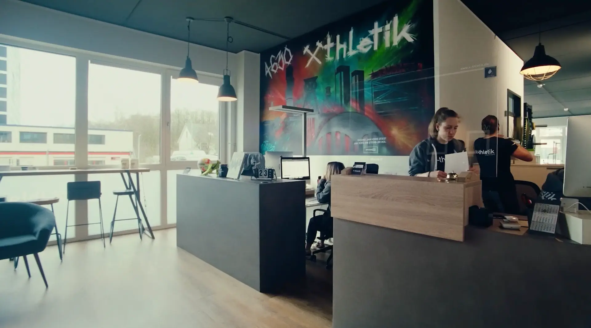 Blick in den Empfangsbereich von x-thletik mit modernem Graffiti-Wandbild und freundlichem Team – Teaserbild zur Praxis auf der Unterseite ‚Physiotherapie‘.
