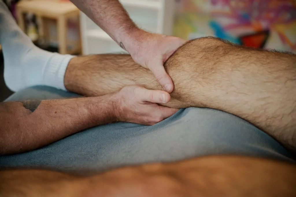 Ein x-thletik-Coach behandelt die Kniekehle eines liegenden Patienten mit gezielten Handgriffen. Das Bild verdeutlicht die Bedeutung physiotherapeutischer Maßnahmen zur Verletzungsprävention im Fußball.