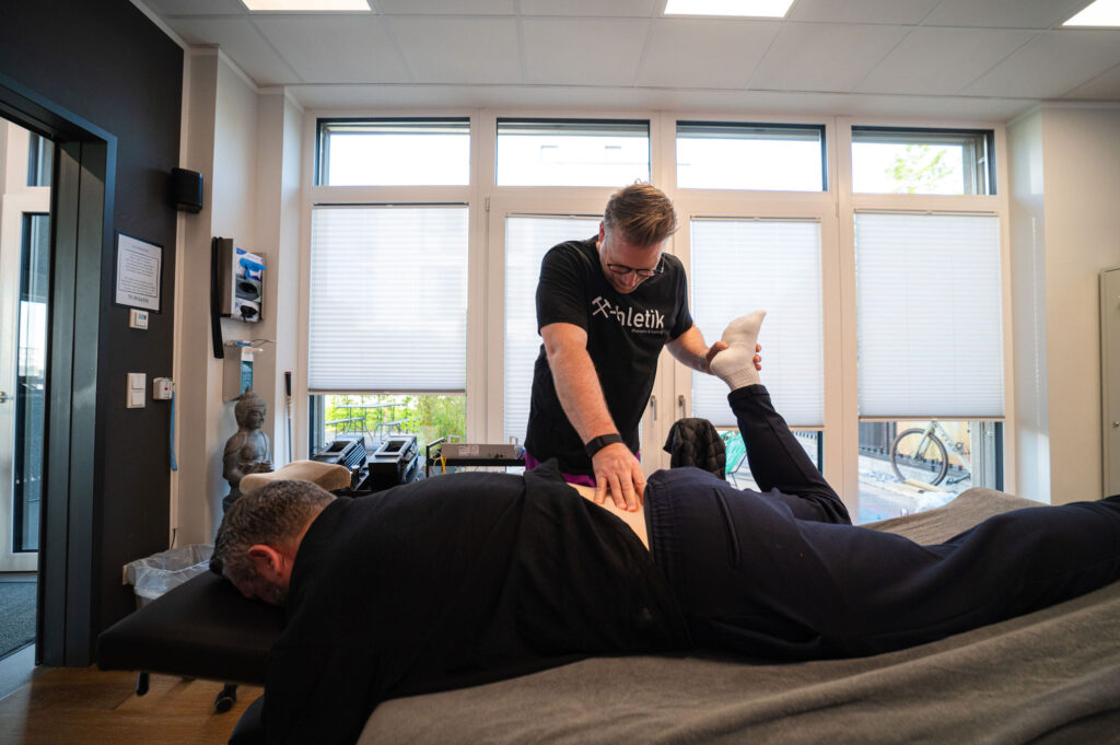 Sebastian Kaul behandelt den unteren Rücken und das Bein eines Patienten auf der Liege in einem hellen Raum bei x-thletik – individuelle manuelle Therapie zur Mobilisation.