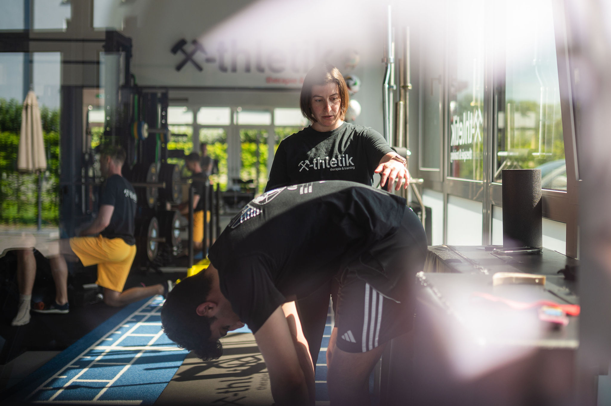 Trainerin von x-thletik begleitet einen Athleten bei einer funktionellen Bewegungsübung im lichtdurchfluteten Trainingsbereich – Beitragsbild der Leistungsseite ‚Road to Performance‘