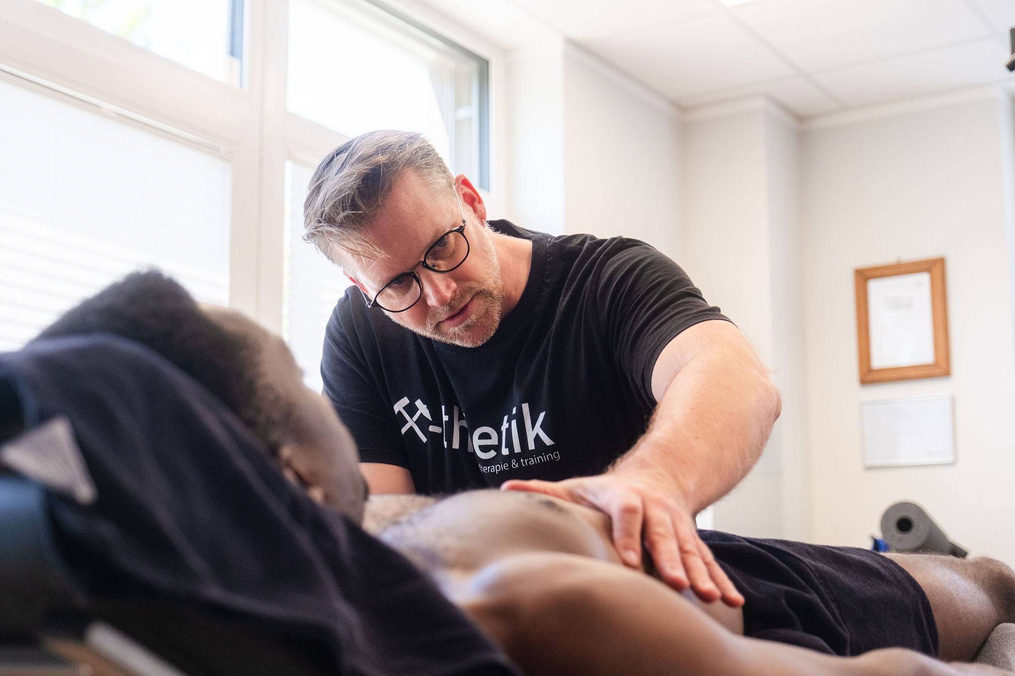 Physiotherapeut Sebastian Kaul behandelt konzentriert den Brustkorb eines Patienten in einem hellen Behandlungsraum von x-thletik – ein Einblick in die individuelle Betreuung im Therapiekonzept.