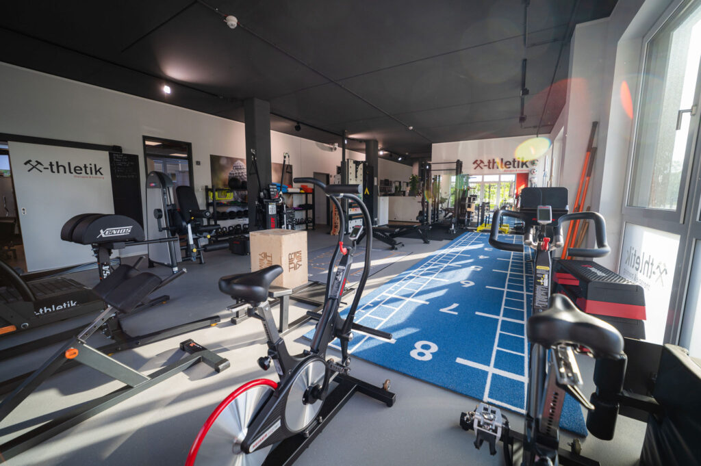 Modern ausgestattetes Fitnessstudio von x-thletik mit verschiedenen Trainingsgeräten, Sprintstrecke und funktionellen Bereichen – Symbol für personalisiertes Training und individuelle Betreuung zum Weltgesundheitstag.